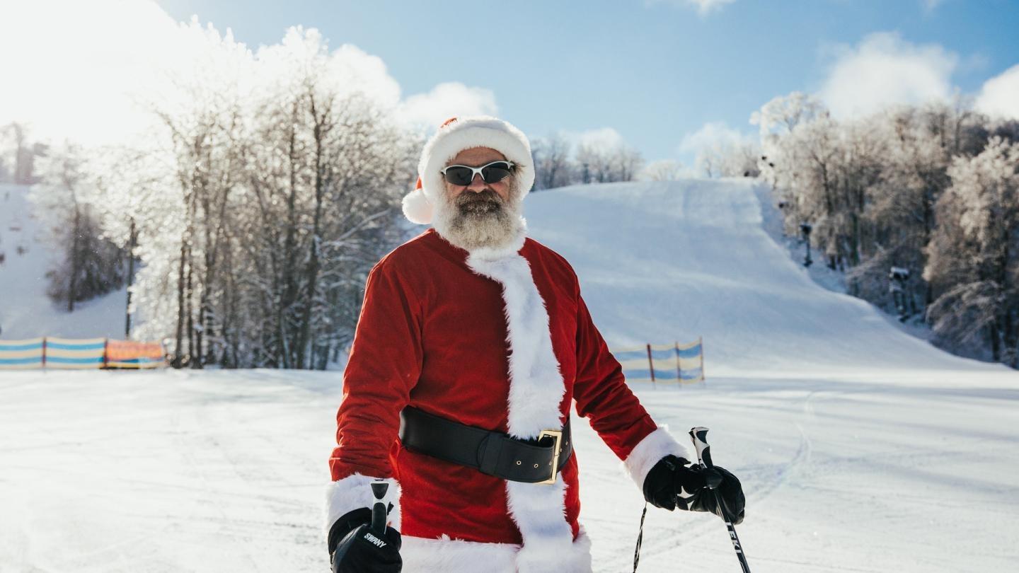 Santa skiing on a snowy hill under a clear blue sky.