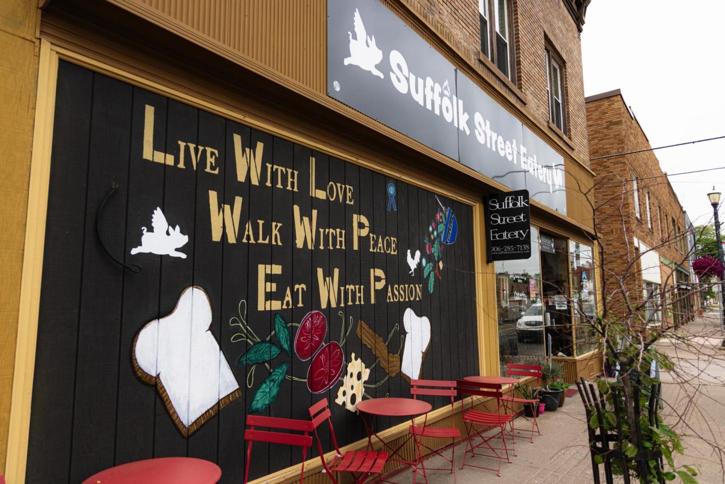 Bakery storefront with mural and outdoor red chairs.