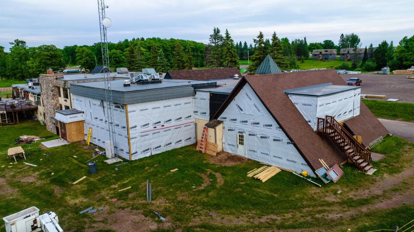 Large building under construction with a brown roof, surrounded by greenery.