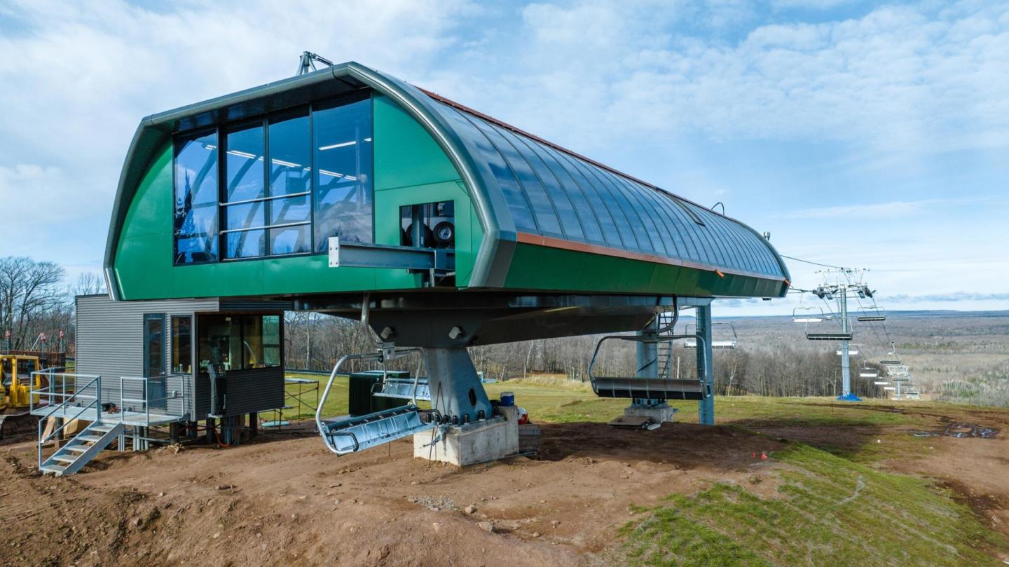 Ski lift station with green and glass exterior under a blue sky.