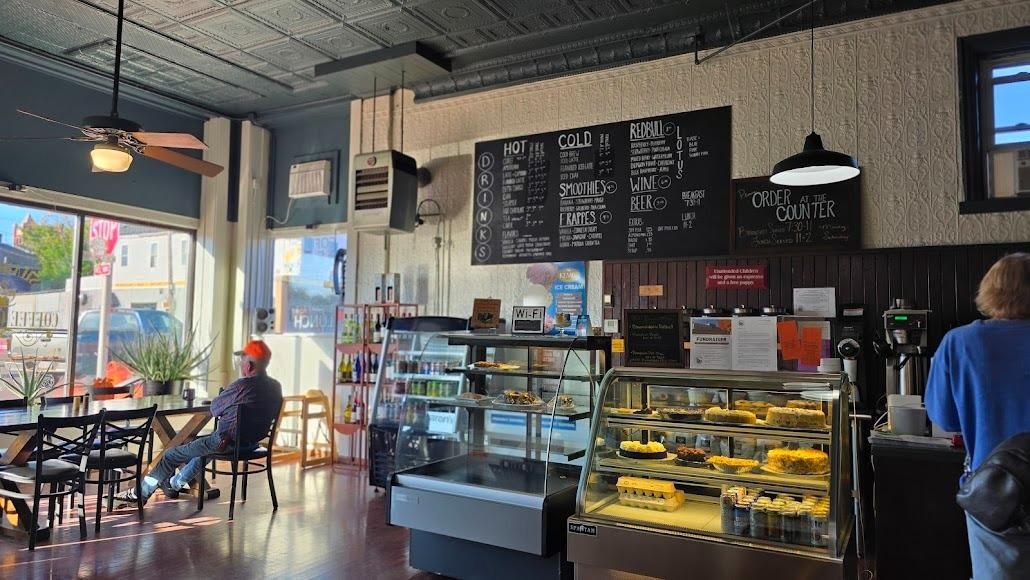 Cozy cafe interior with display cases, menu boards, and patrons seated near windows.