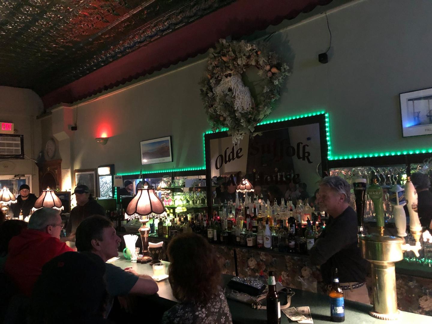 Dimly lit bar with people seated, bartender serving drinks.