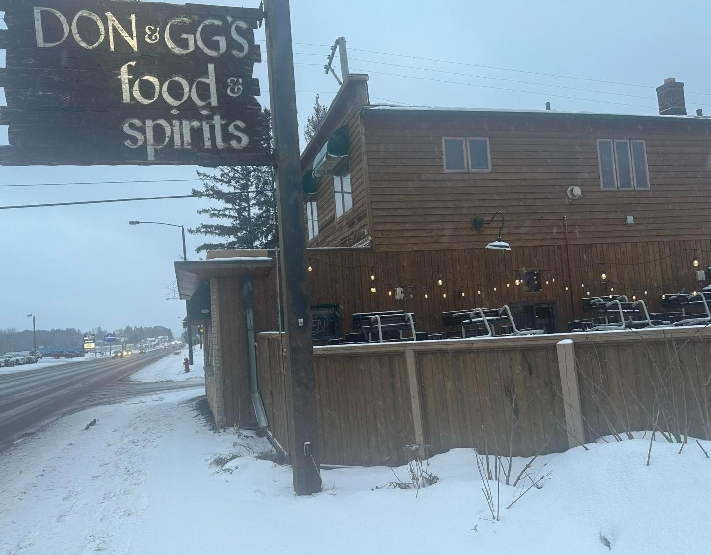 Snowy street view of a wooden restaurant with sign, "Don & GG's Food & Spirits."