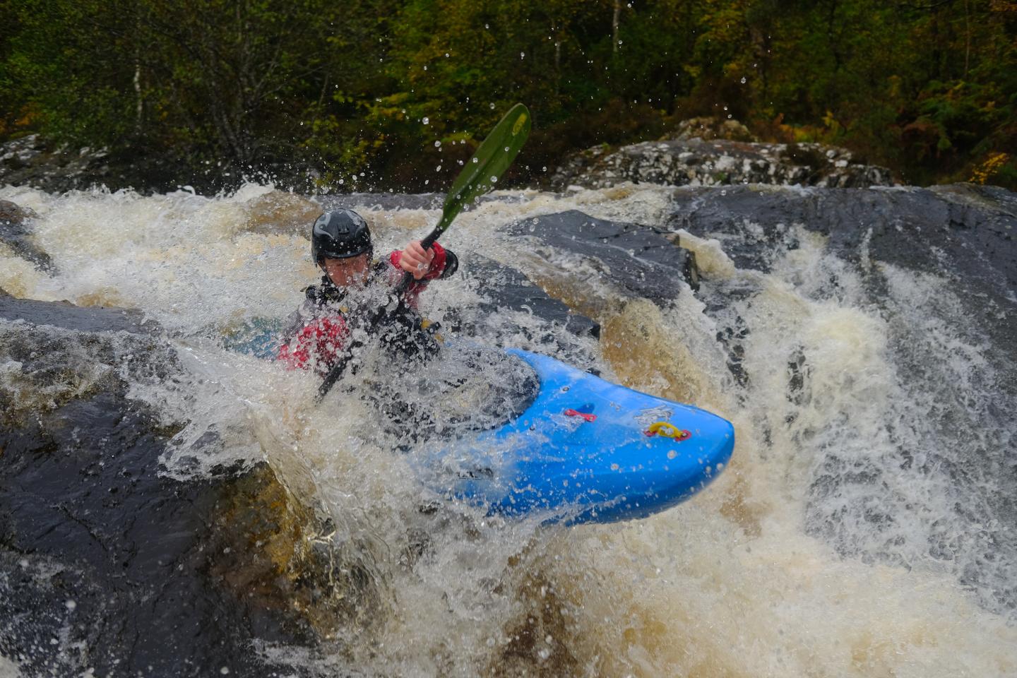 Kayaker navigating a waterfall in a blue kayak, surrounded by rushing water.