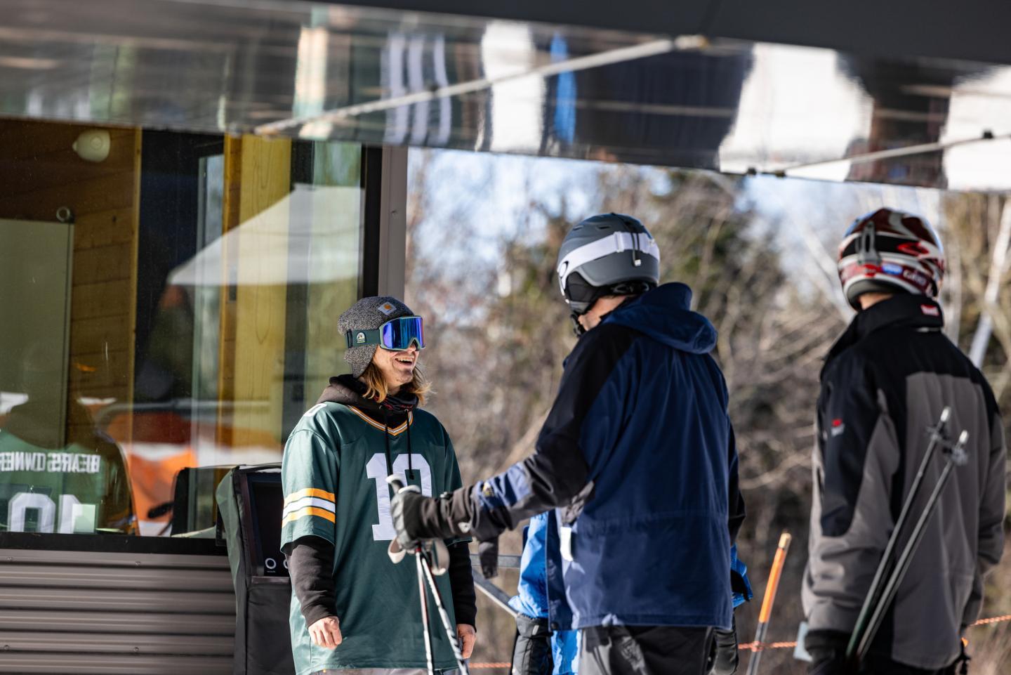 Skiers in gear chatting outside a ski lodge, wearing helmets and goggles.