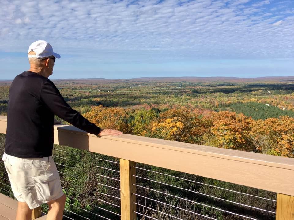 Man on a deck overlooking a colorful autumn forest.