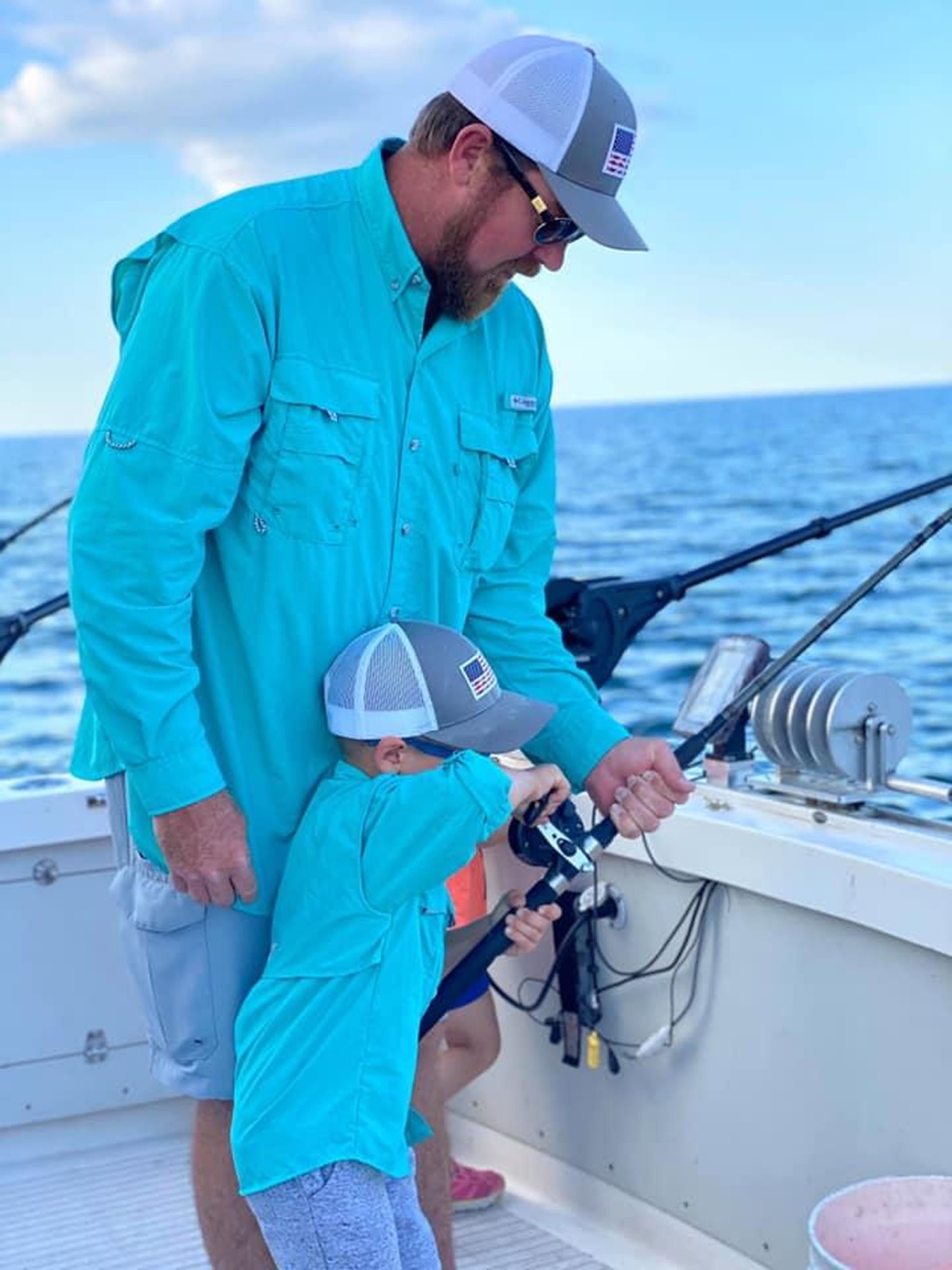 Father and child fishing on a boat under a clear blue sky.