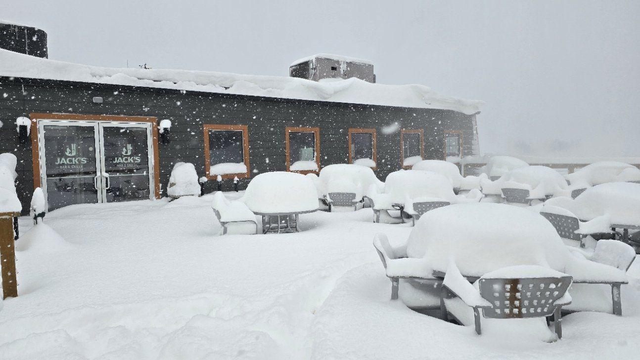 Snow-covered outdoor patio with chairs and tables, heavy snowfall.