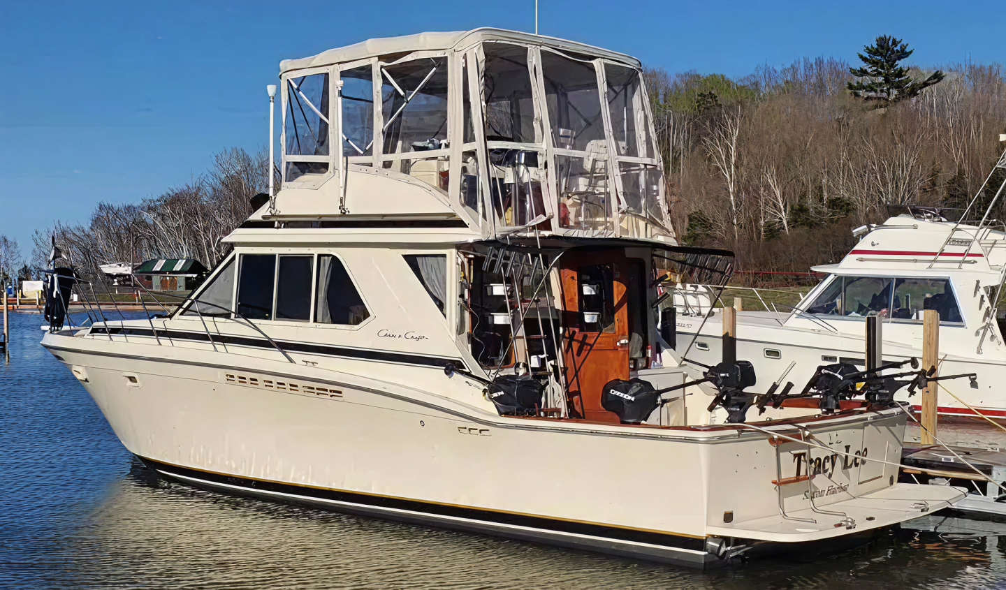 A beige cabin cruiser docked by the water with trees in the background.
