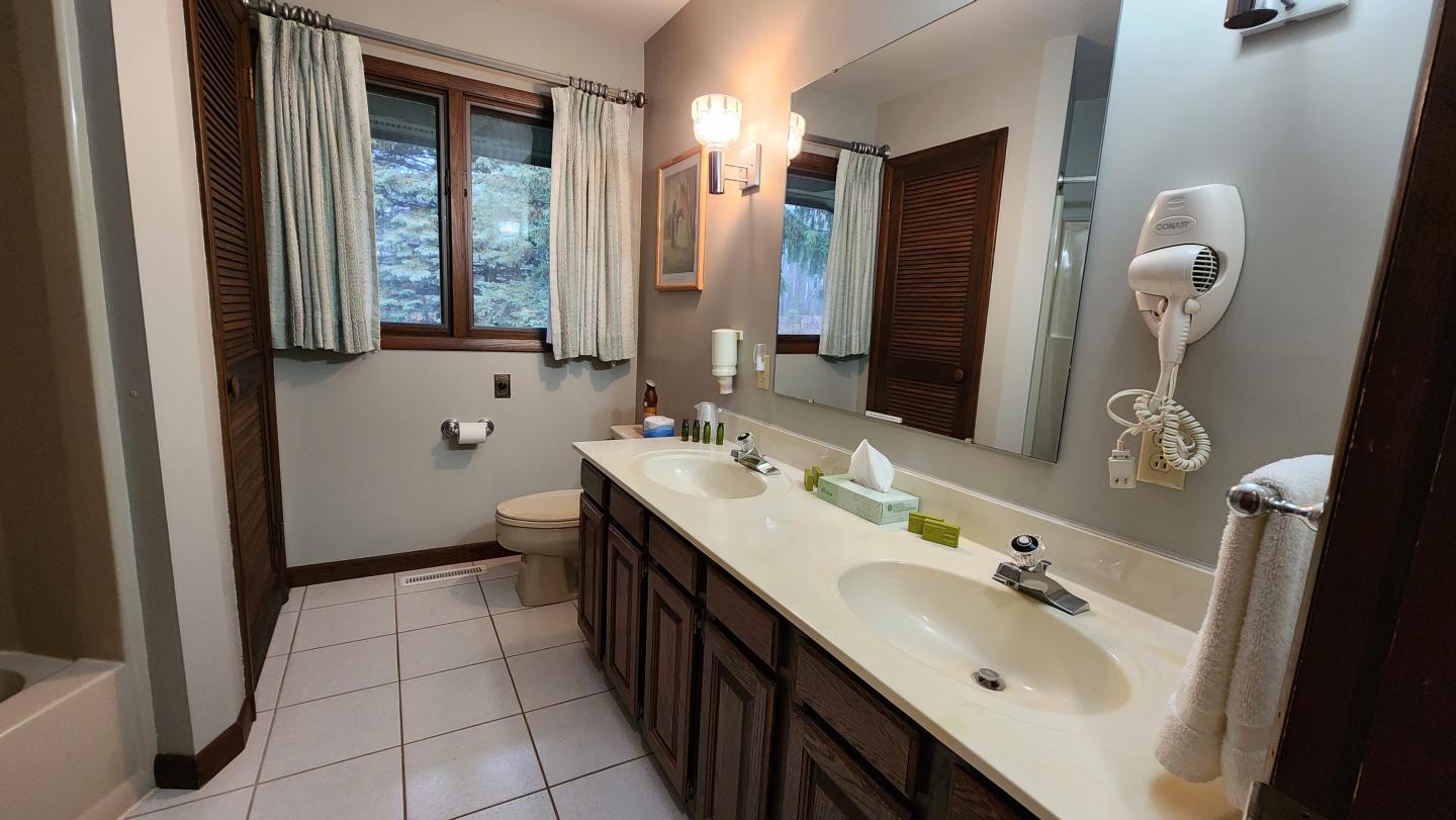Bathroom with double vanity, large mirror, and window with curtains.