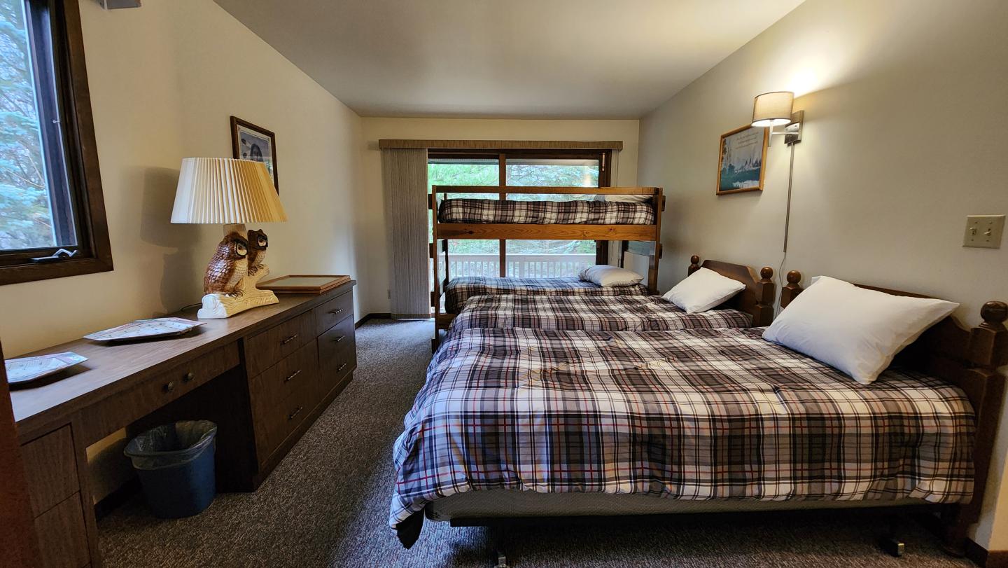Cozy bedroom with a double bed, bunk bed, desk, and lamp. Neutral tones.