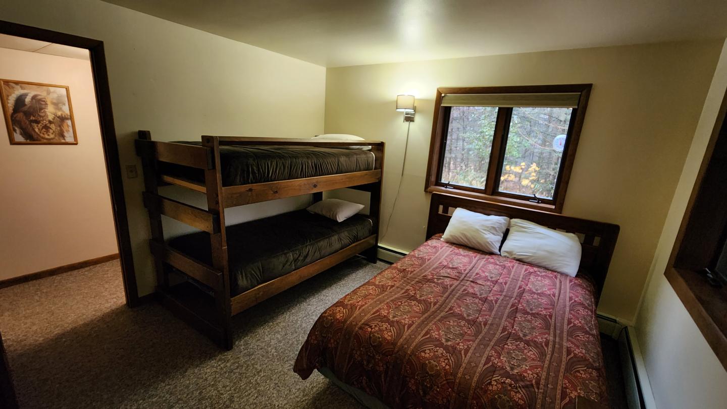 Cozy bedroom with bunk bed, a double bed, and a window showing trees.