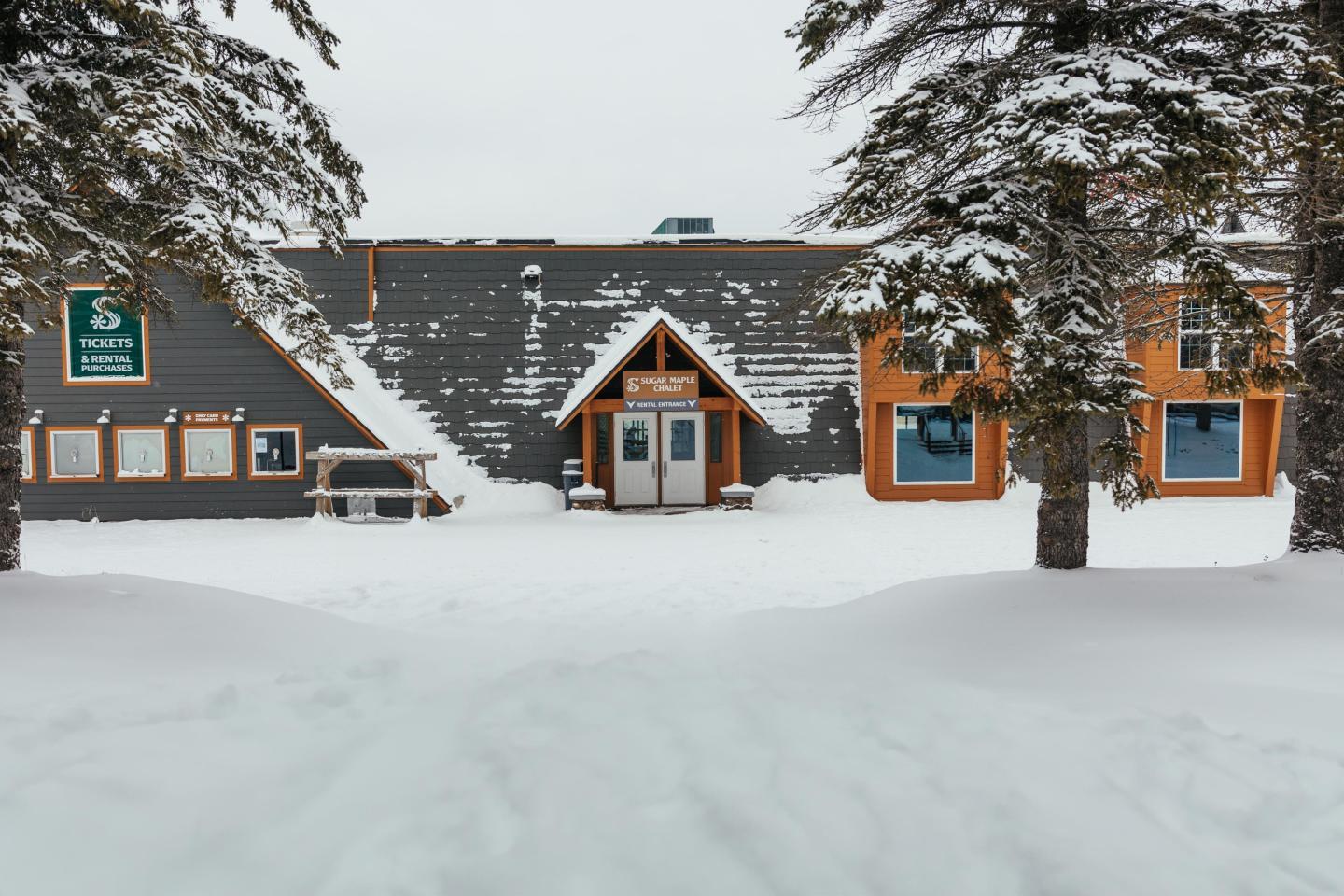 Snow-covered lodge with pine trees and an A-frame entrance.