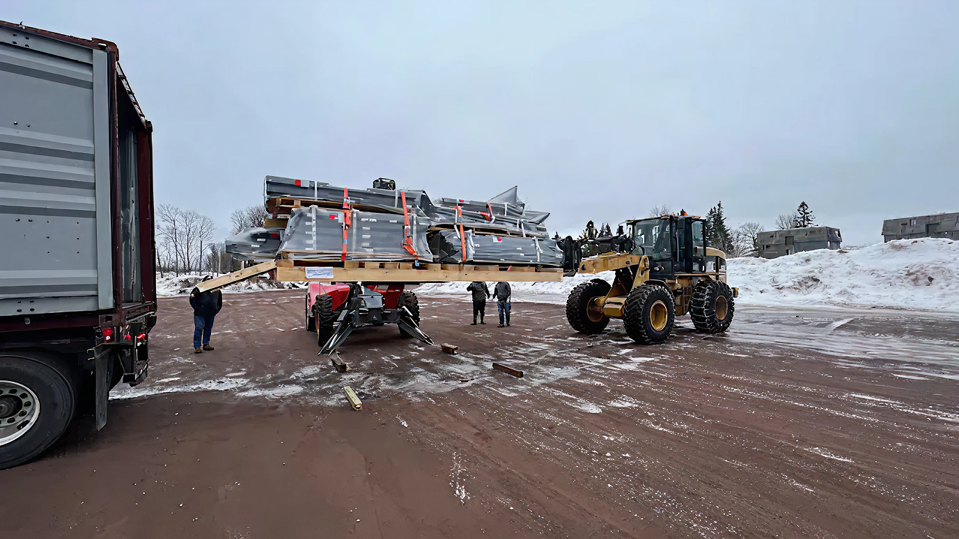 Forklift moving metal beams in a snowy industrial yard.