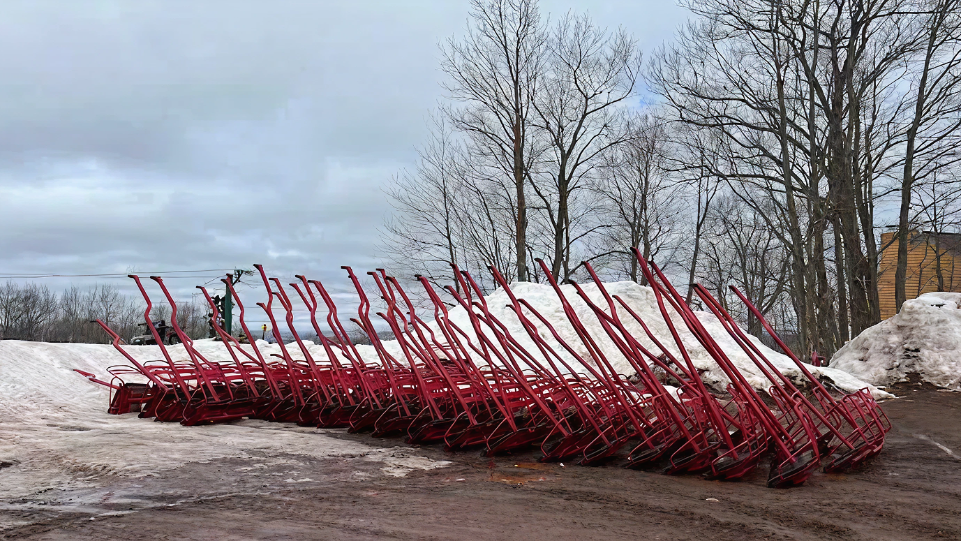 Red sleds stacked in rows on snowy ground, trees in the background.