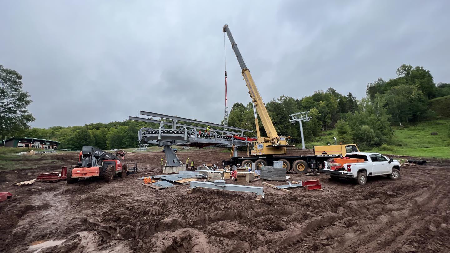 Construction site with crane and trucks on a muddy field under gray sky.