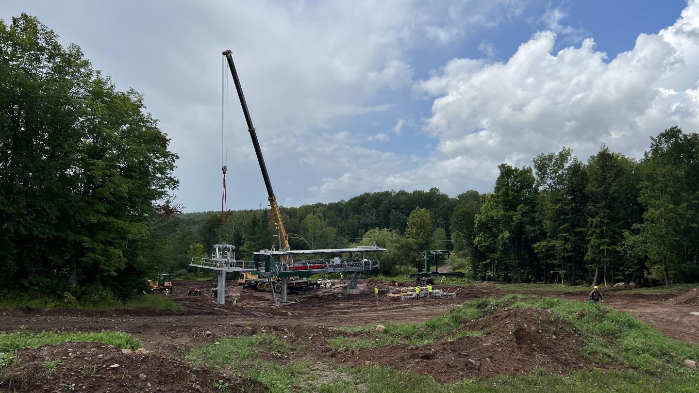 Construction site with crane and workers in a grassy area under a cloudy sky.