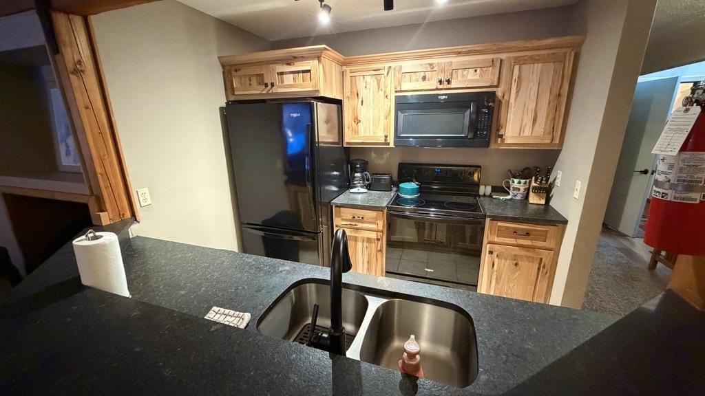 Cozy kitchen with wooden cabinets, black appliances, and a central sink.