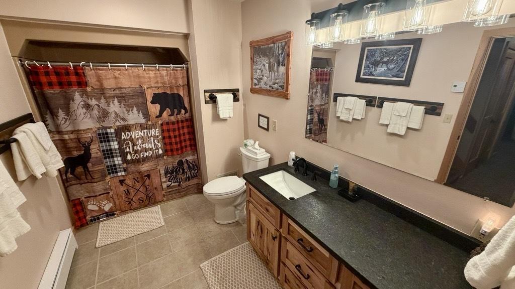 Rustic bathroom with bear-patterned shower curtain, dark countertop, and soft lighting.