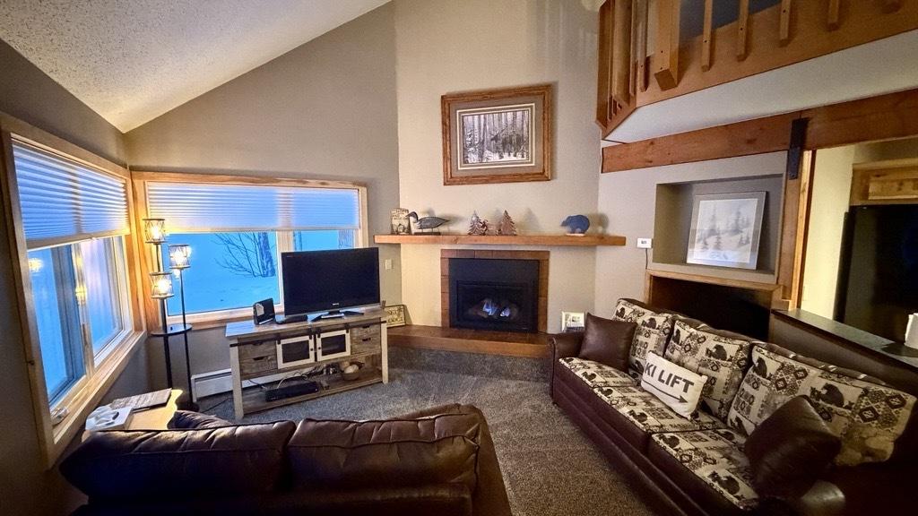 Cozy living room with sofas, TV, fireplace, and large window. Wood and earth tones dominate.