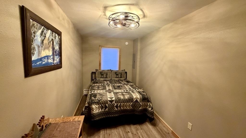 Narrow bedroom with a bed, patterned cover, painting, and overhead light.