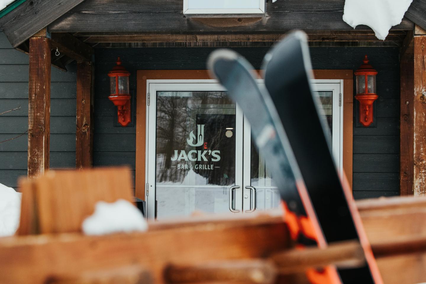 Ski lodge entrance with skis in foreground, snow on roof.