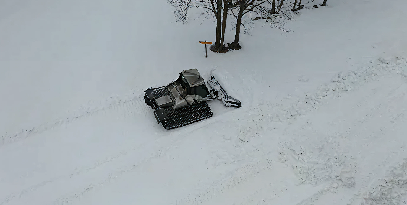Snow-covered vehicle parked near trees on a snowy landscape.