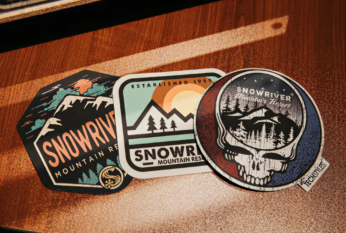 Three Snowridge mountain-themed stickers on a wooden surface.