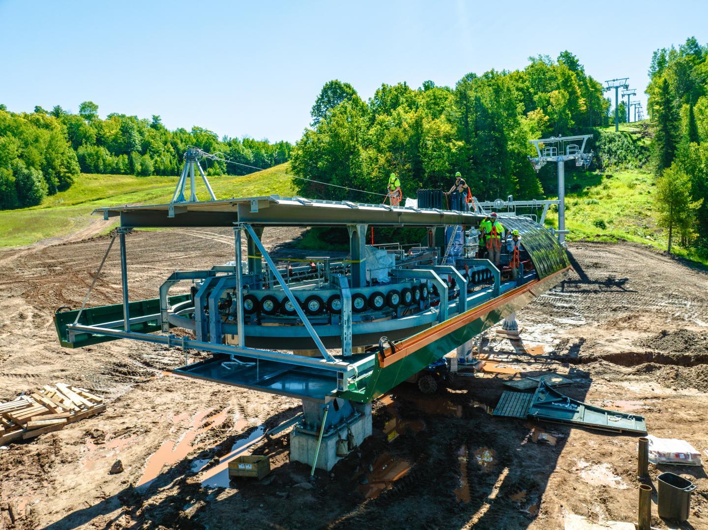 Construction of a ski lift in a wooded area under a clear blue sky.