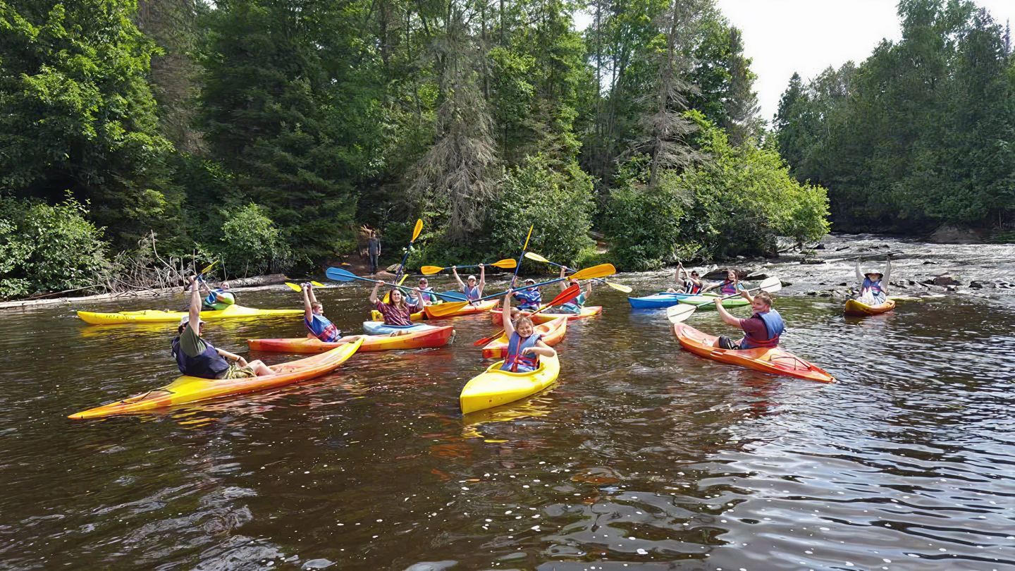 Kayakers paddling on a river surrounded by lush green trees.