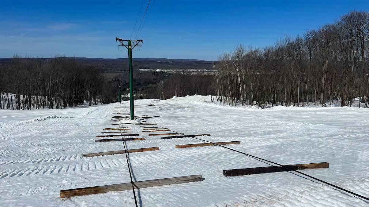 Snowy ski slope with a lift and blue sky.