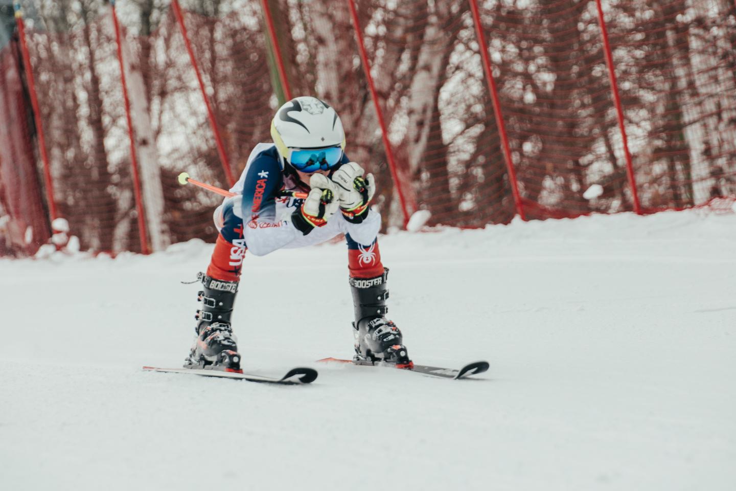 Child in ski gear racing downhill, snowy background.