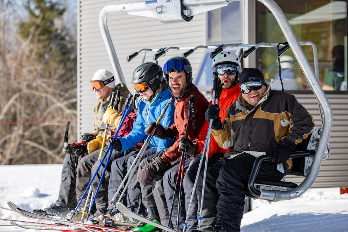 Skiers sitting on a lift, smiling on a sunny day.