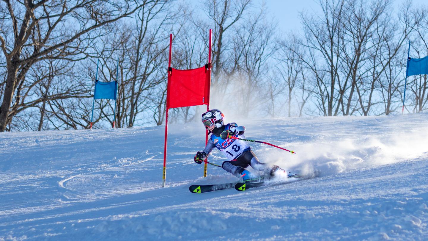 Skier racing downhill past a red slalom gate on a snowy slope.