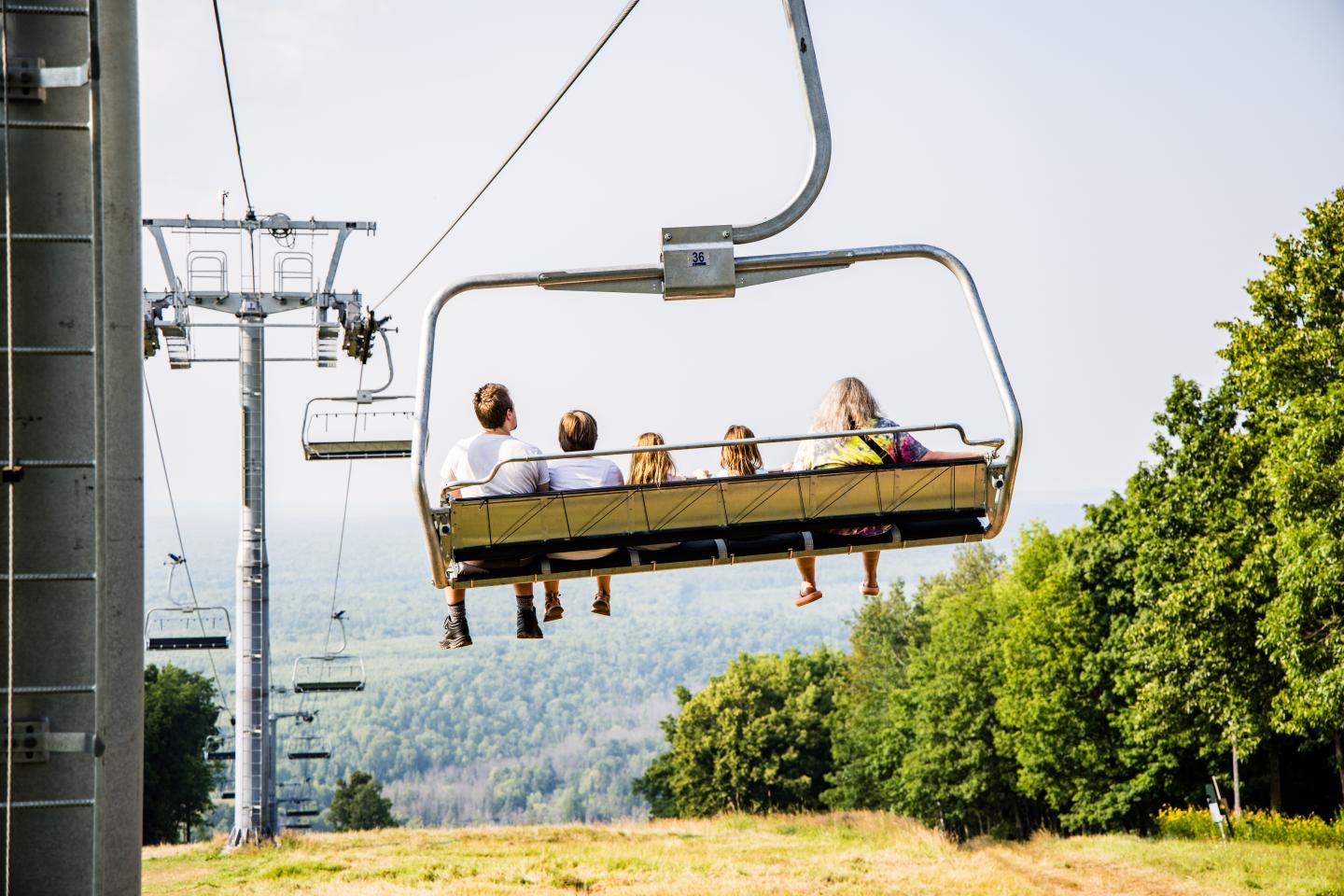 Chairlift carrying people over a green landscape under a clear sky.