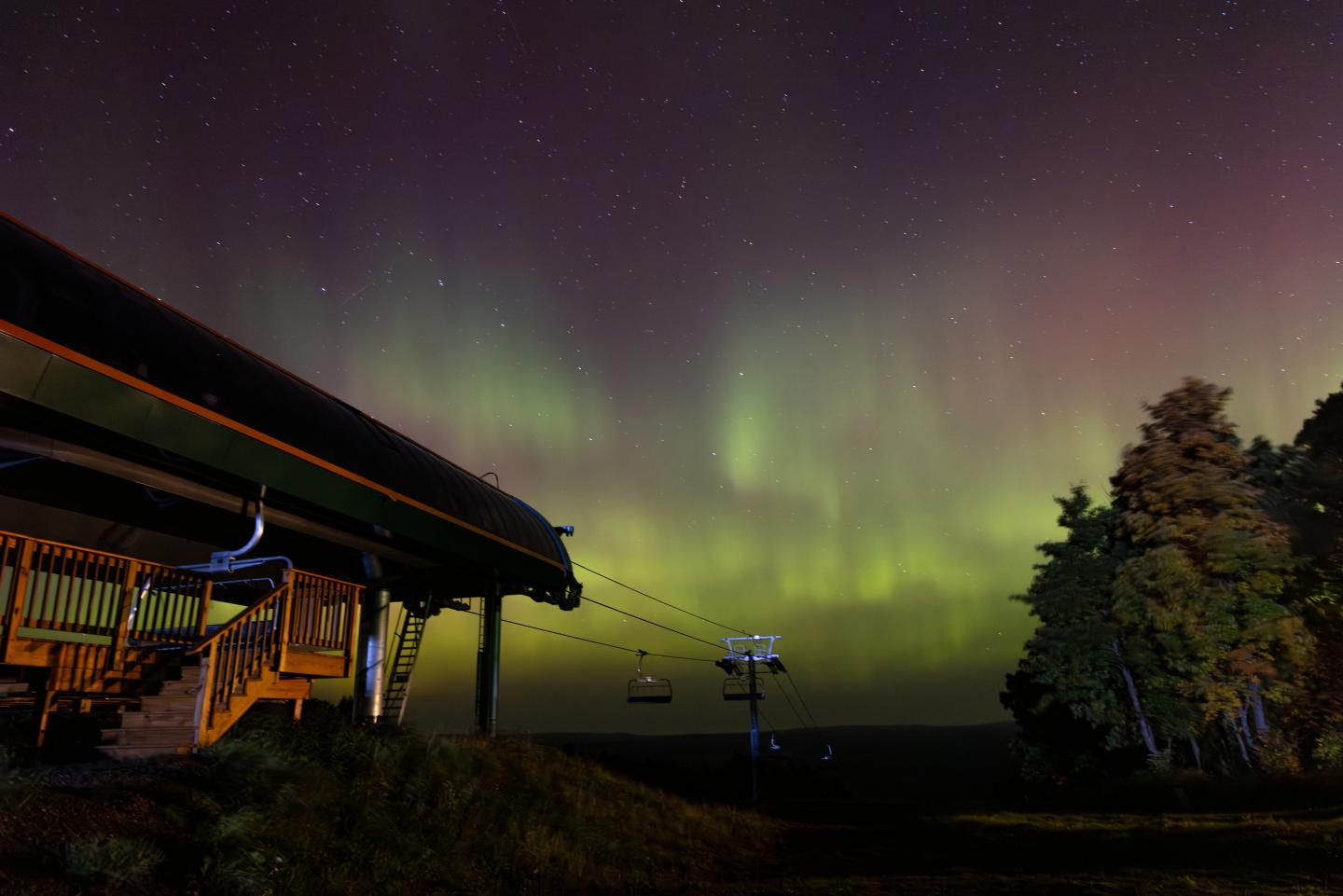 Northern lights over ski lift, vibrant green hues against starry sky.