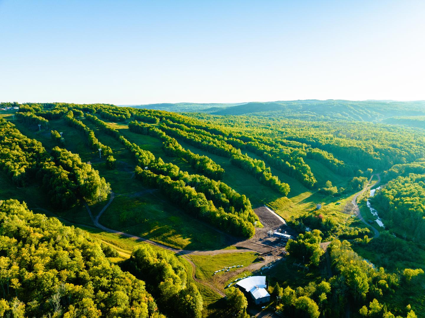Aerial view of green hills and a winding road under a clear blue sky.