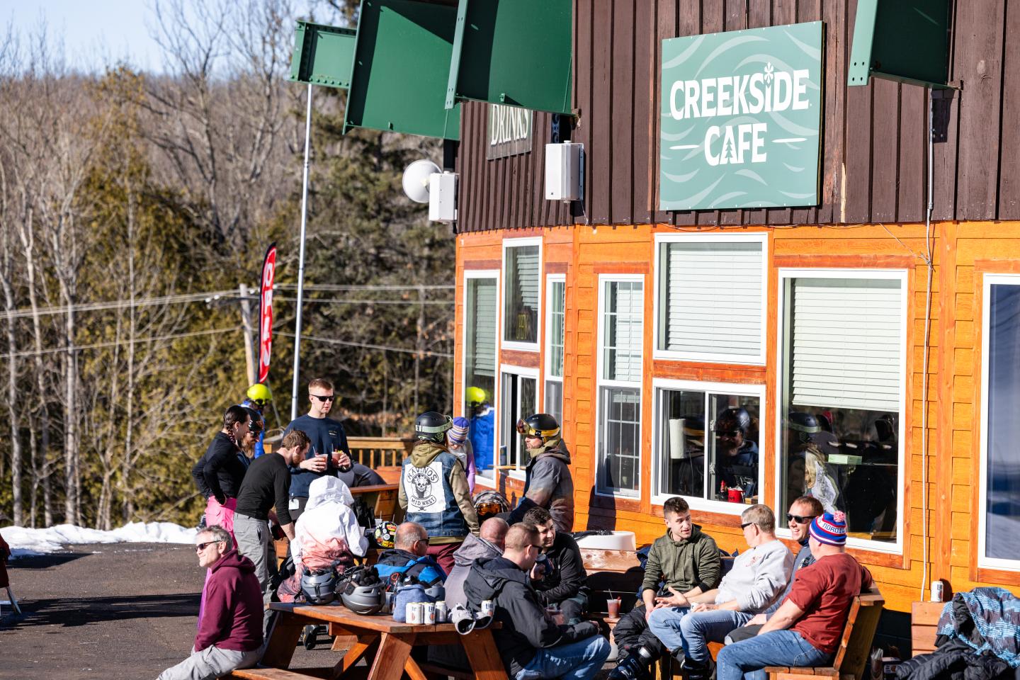 People relax outside a cafe, surrounded by trees, on a sunny day.