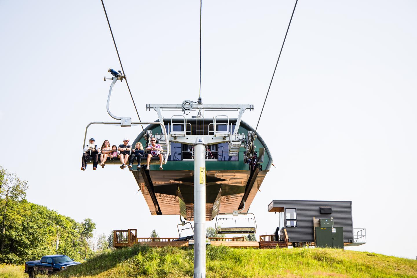 Ski lift with people ascending a grassy hill under a clear sky.