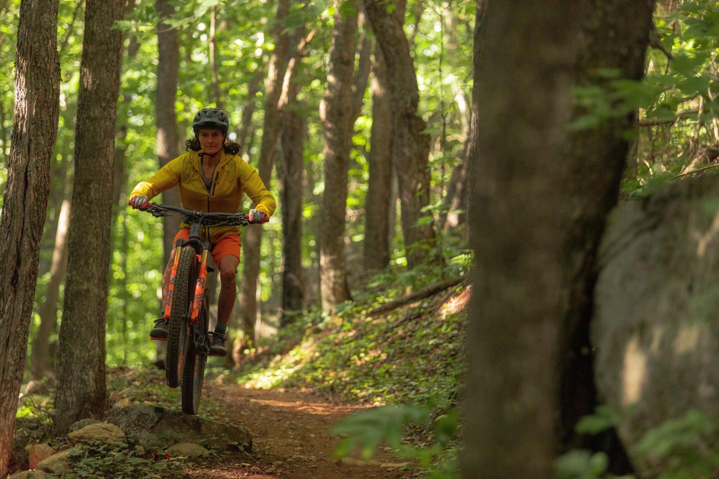 Mountain biker on forest trail, wearing yellow shirt and helmet.