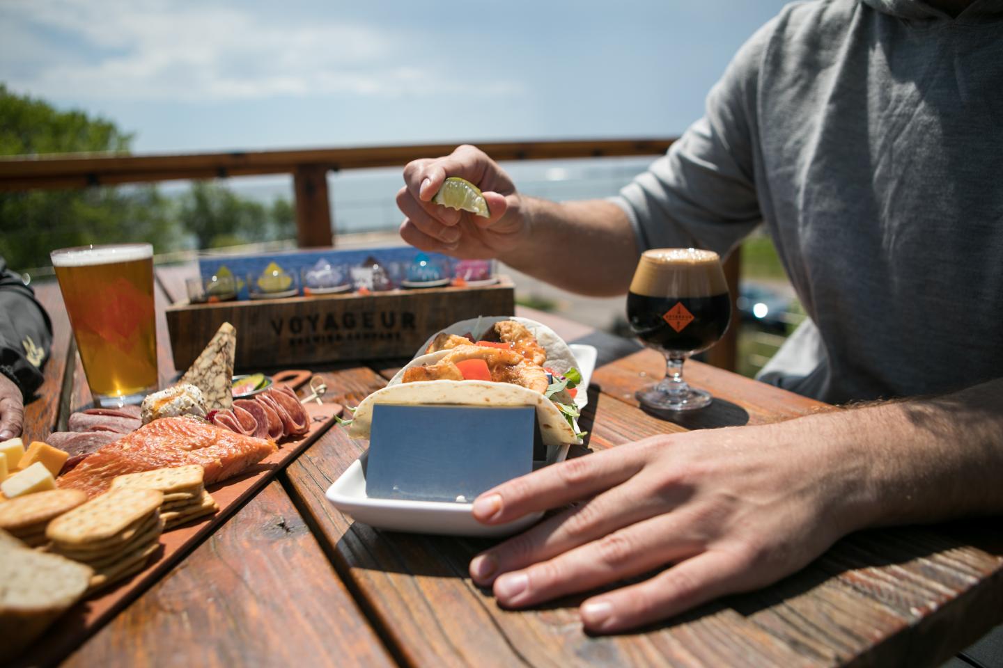 Man squeezes lime over a seafood dish on a sunny patio table.