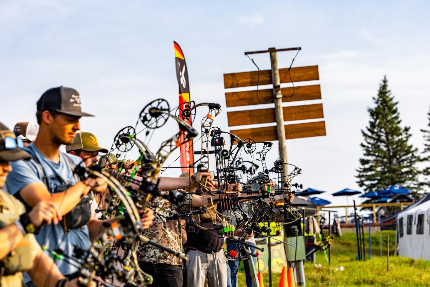 Archers aiming their compound bows outdoors under a bright sky.