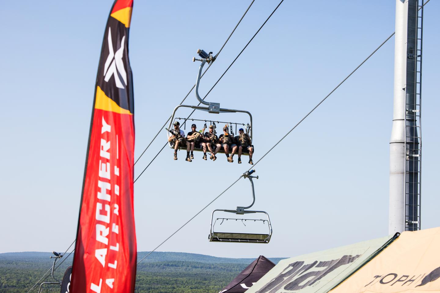 Ski lift with people above tents under a clear sky.