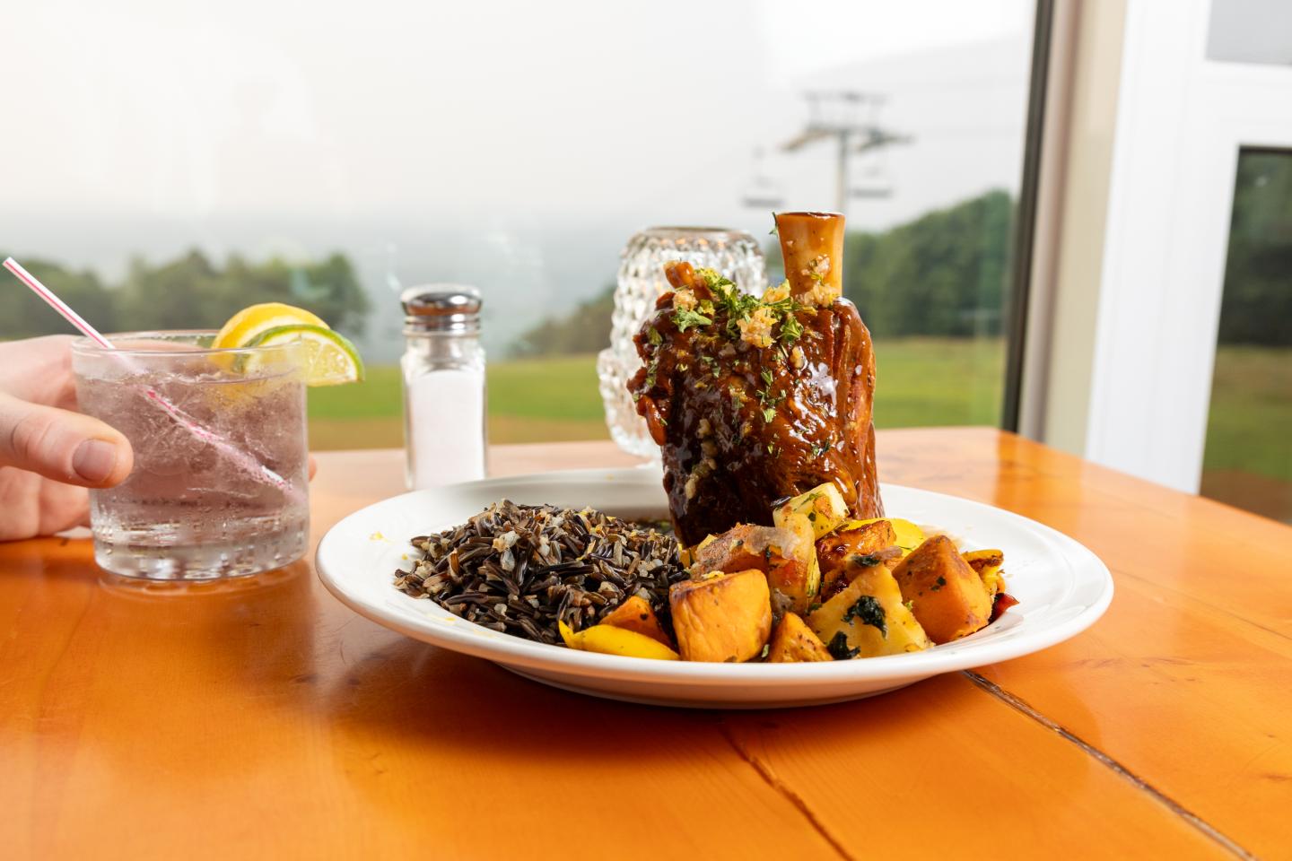 Braised lamb shank with grains and roasted vegetables on a white plate.