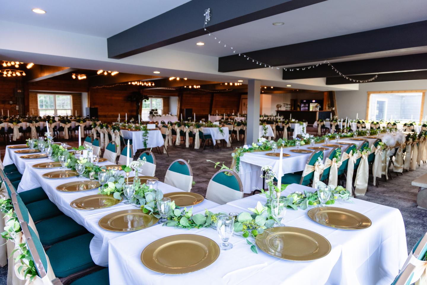 Elegant banquet hall with tables set for an event, adorned with greenery.