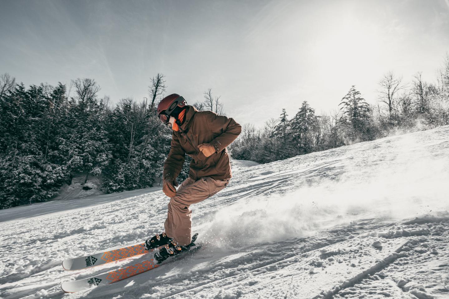 Skier in motion on snowy slope under bright sky, wearing helmet and goggles.