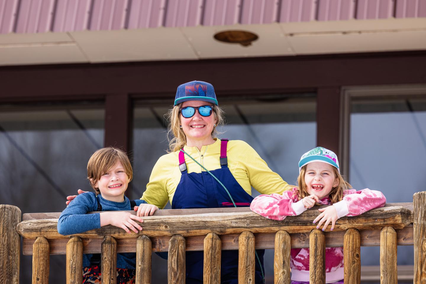 Woman and two children smiling on a wooden balcony.