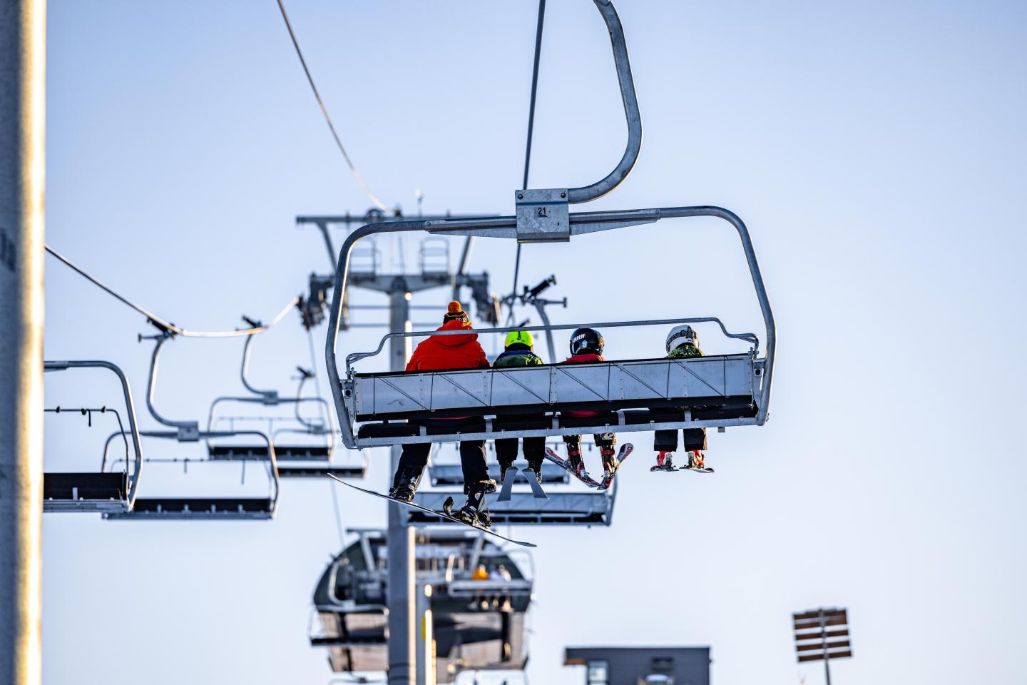 Ski lift with three people ascending, clear blue sky.