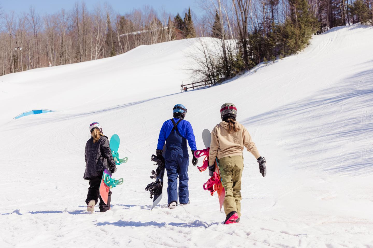 Three people walking uphill with snowboards on a snowy slope.