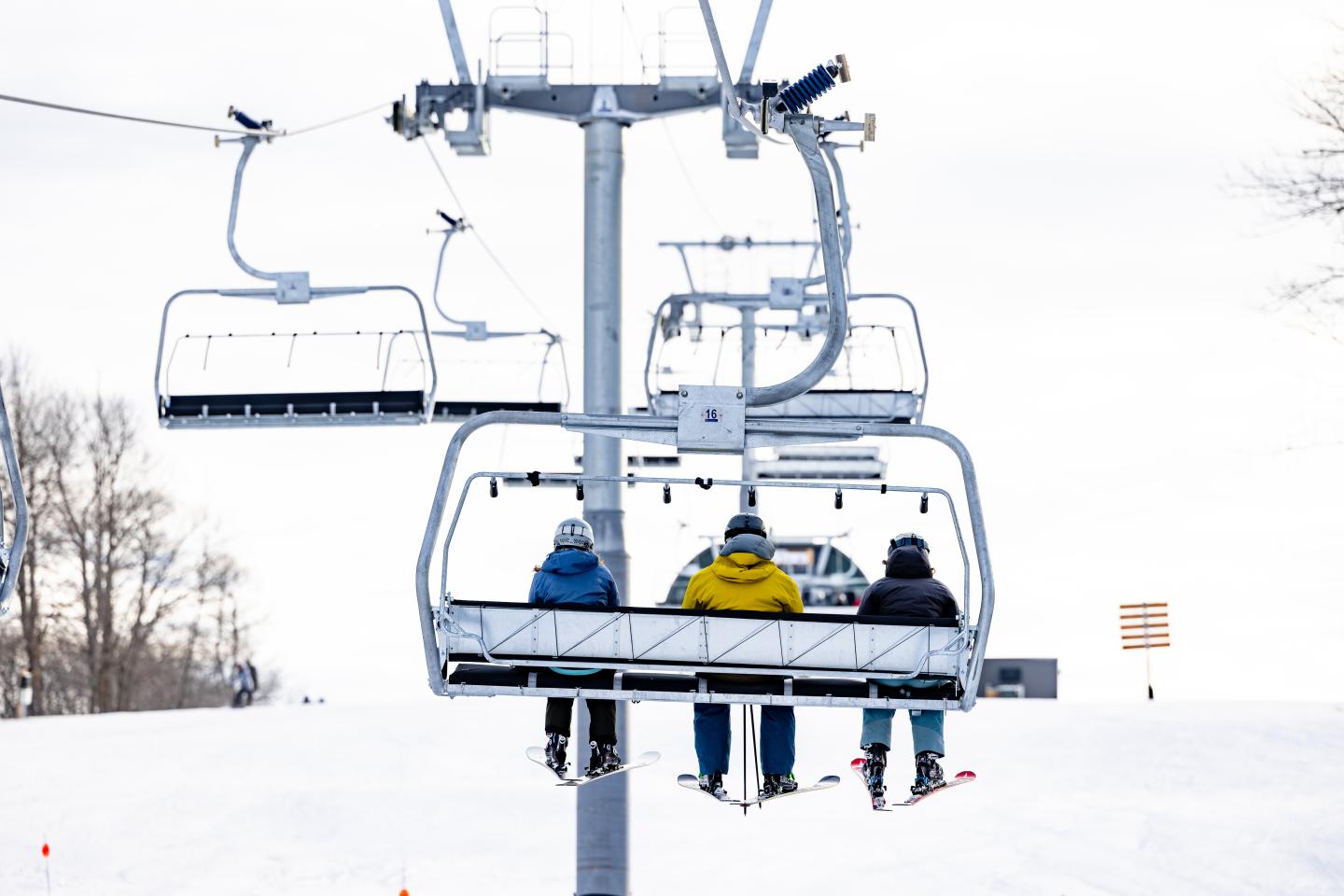 Skiers on a chairlift ascending a snowy slope.